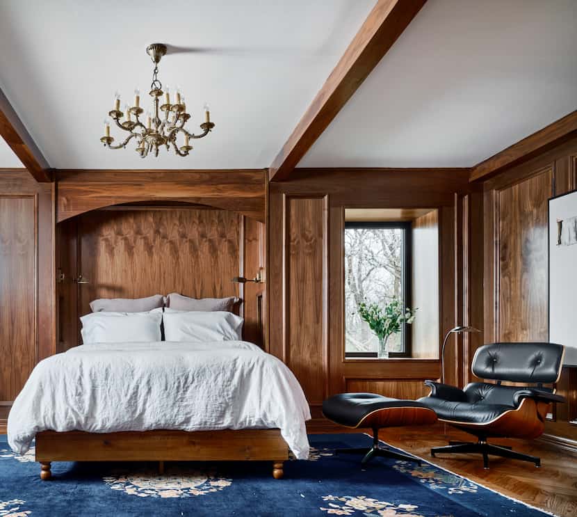 Wood paneling on the walls of a bedroom with a bed at the center, a blue rug beneath the bed...