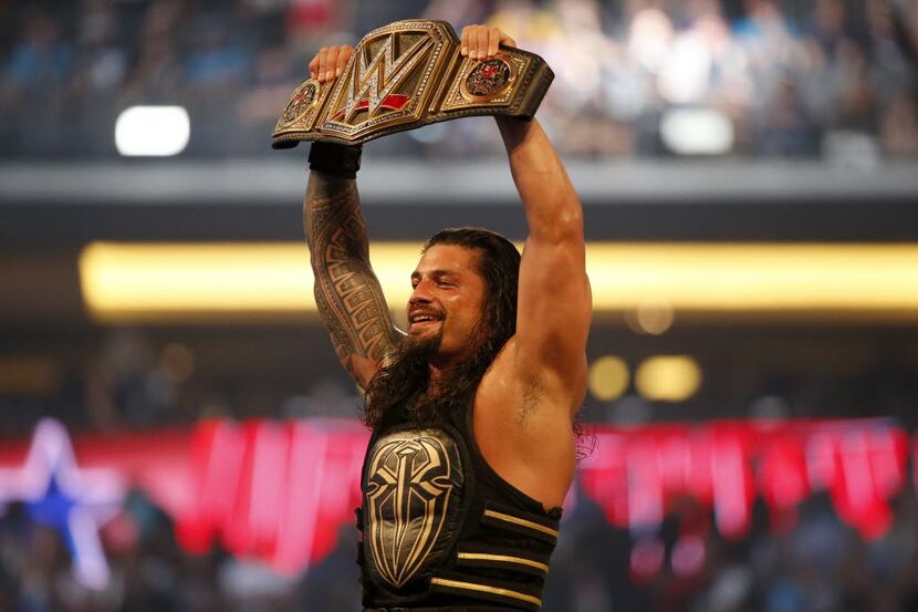 Roman Reigns holds up the championship belt after defeating Triple H during WrestleMania 32...