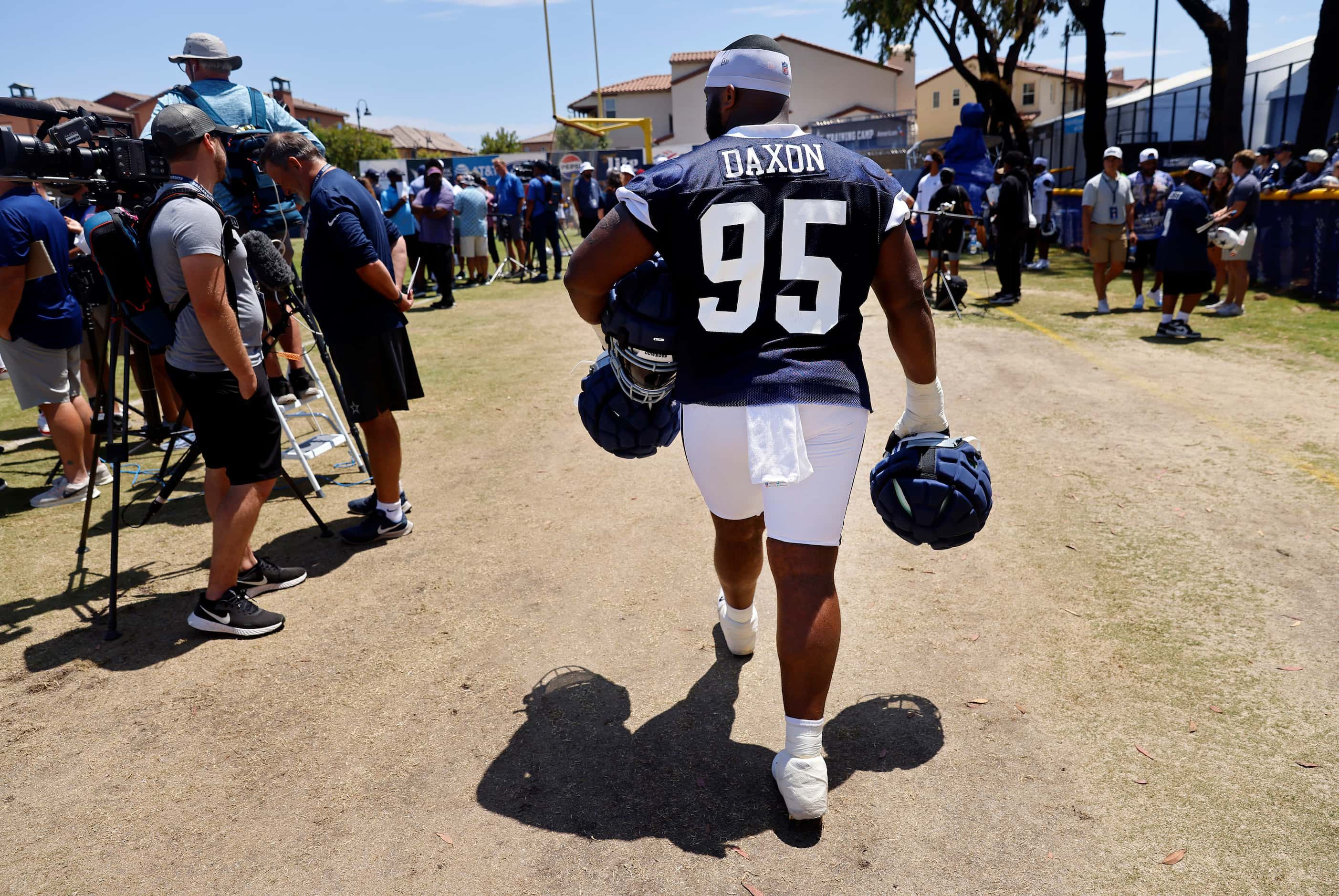 Dallas Cowboys rookie defensive tackle Denzel Daxon (95) carries veteran players helmets to...