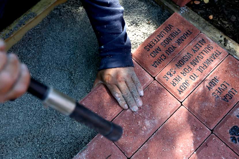 Alex Lira works to install commemorative engraved bricks that were sold to raise funds for...