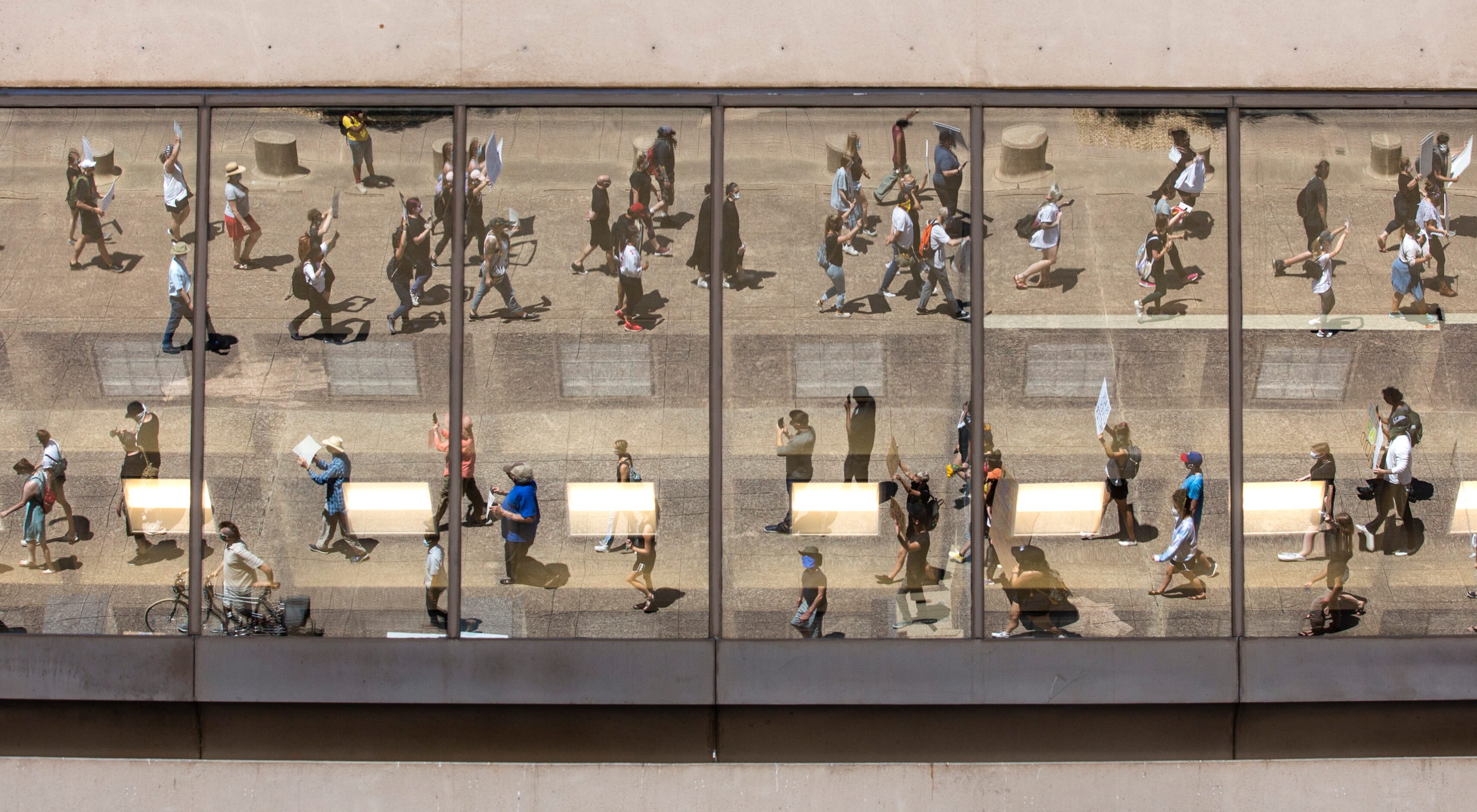 Protesters, reflected in the windows of Dallas City Hall, march in a silent demonstration to...