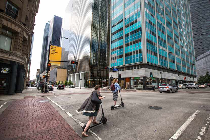 People ride electric scooters in downtown Dallas.