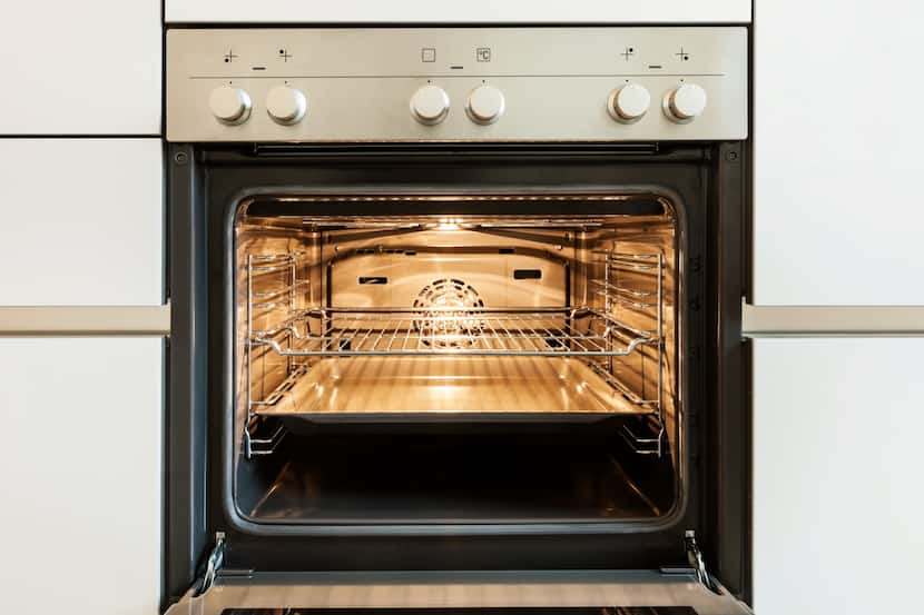 Clean oven with silver control panel and open door, nestled in white cabinets