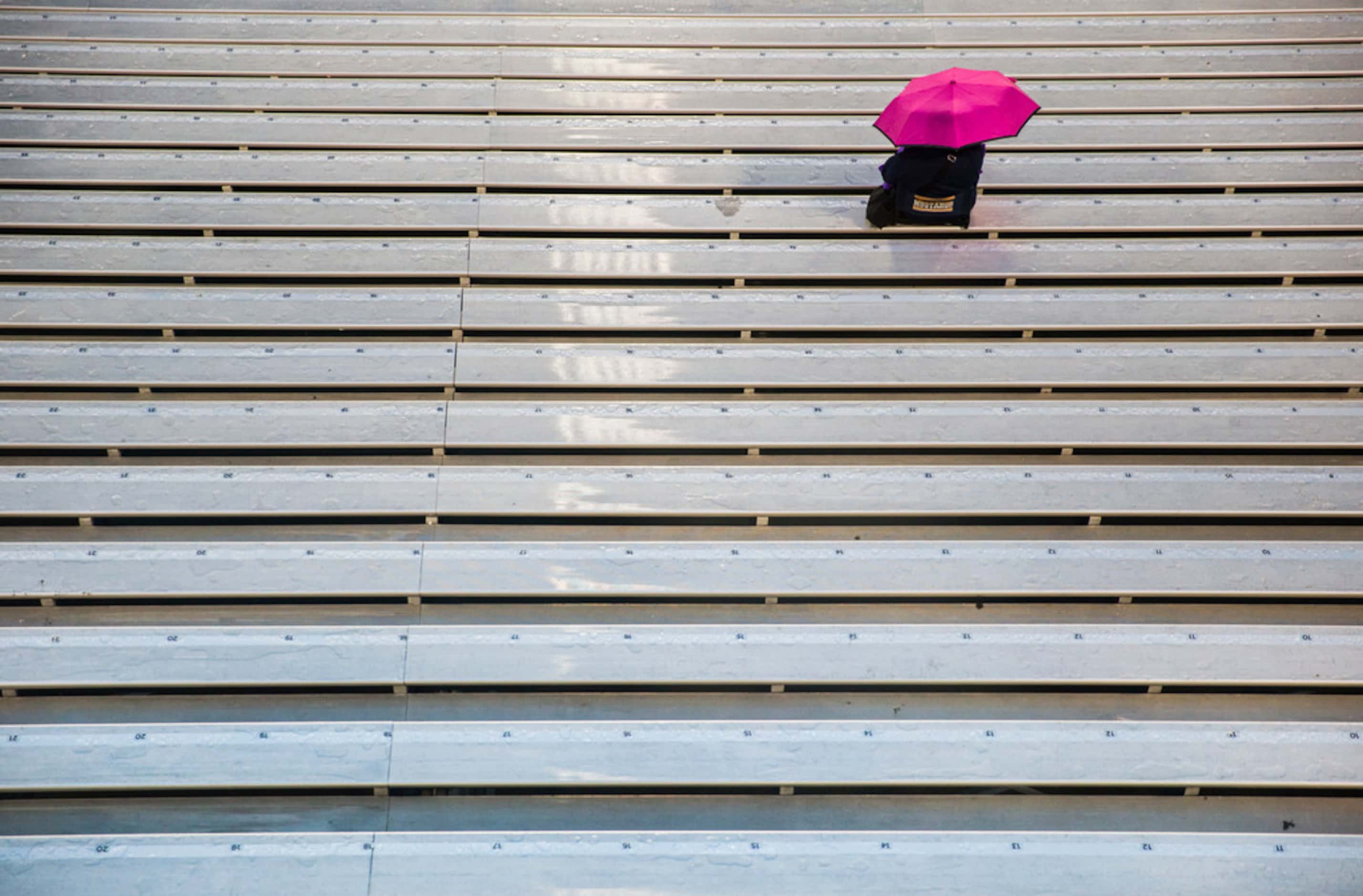 A lone football fan sits in the stands with a pink umbrella before a District 10-6A high...