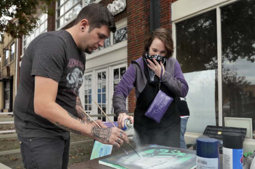 Graffit artist Jason MacGregor helps keep the stencil steady for Amber Caceres as she spray...