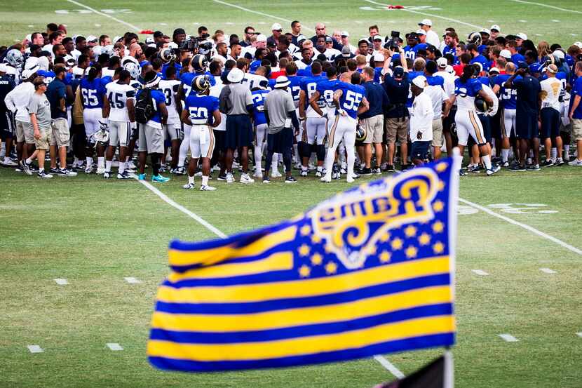 The Dallas Cowboys, in white, and St. Louis Rams, in blue, huddle together before a joint...