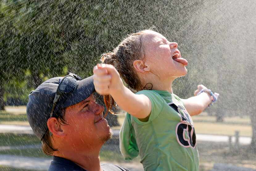 Stormie Thornton, 7, cools off with water sprayed by a mister while her father Clay Thornton...