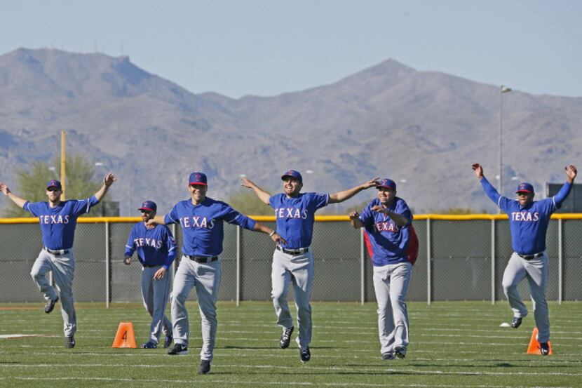 Rangers pitchers and catchers loosen up in the shadow of the Arizona mountains as they...