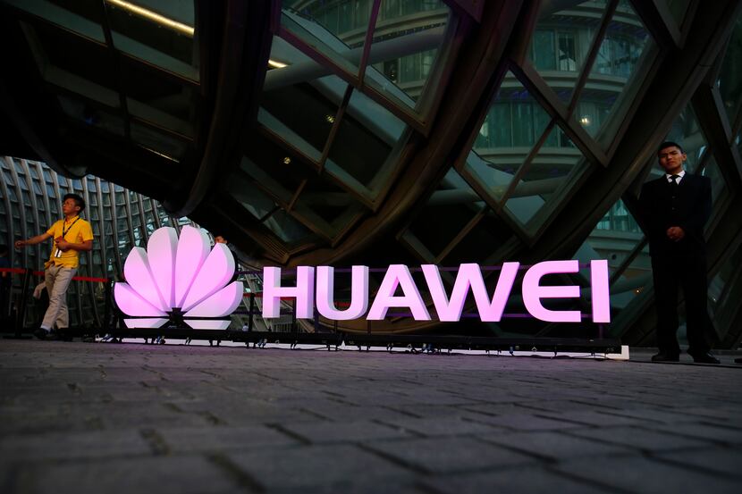 People walk past an illuminated logo for Huawei at a launch event for the Huawei MateBook in...