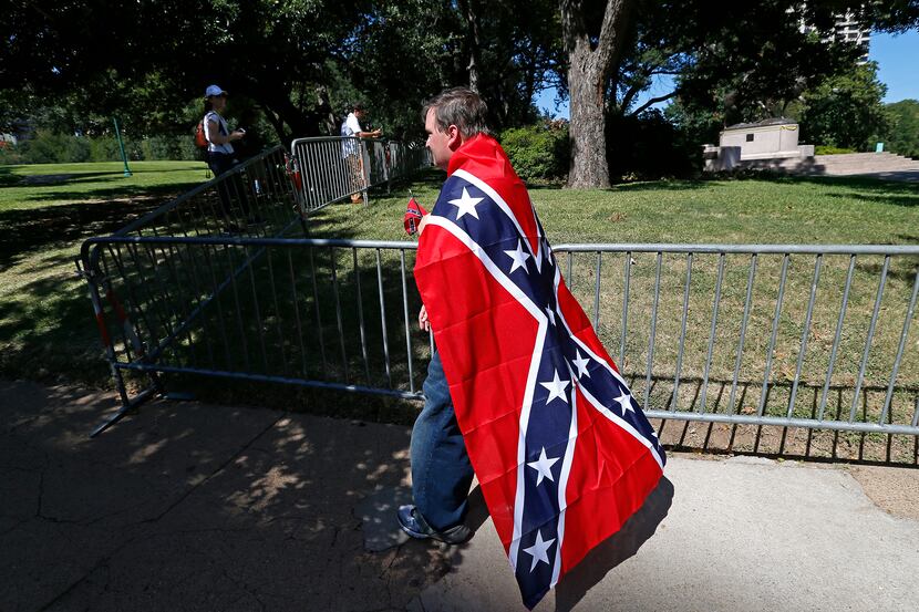 William Rutledge III, wrapped in a Confederate flag, walks on North Hall Street near the...