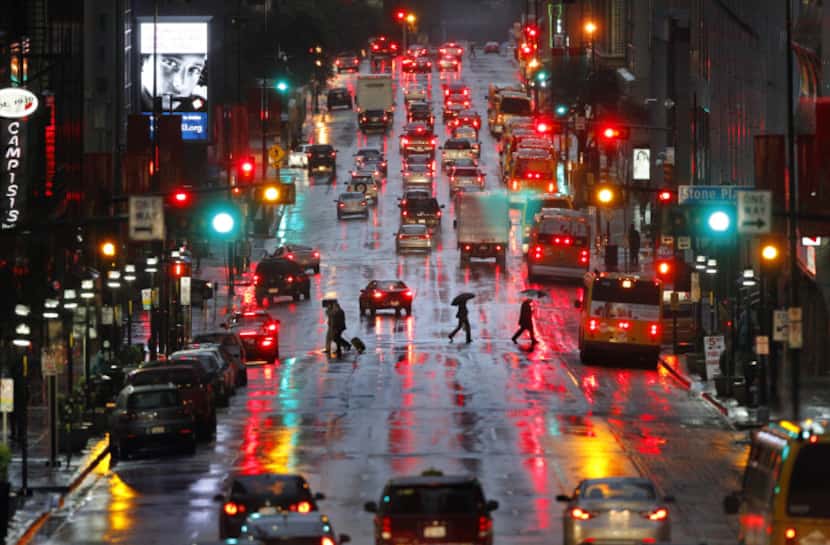 Workers hustle home with umbrellas across Elm Street in downtown Dallas during evening rush...