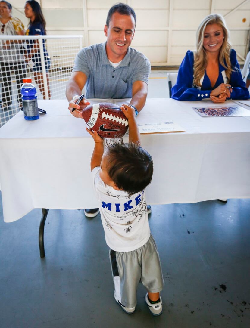 Dallas Cowboys kicker Dan Bailey autographs a football for 18-month-old Mikey Robinson as...