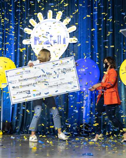 A woman holds a large check at The Pitch with confetti and balloons.