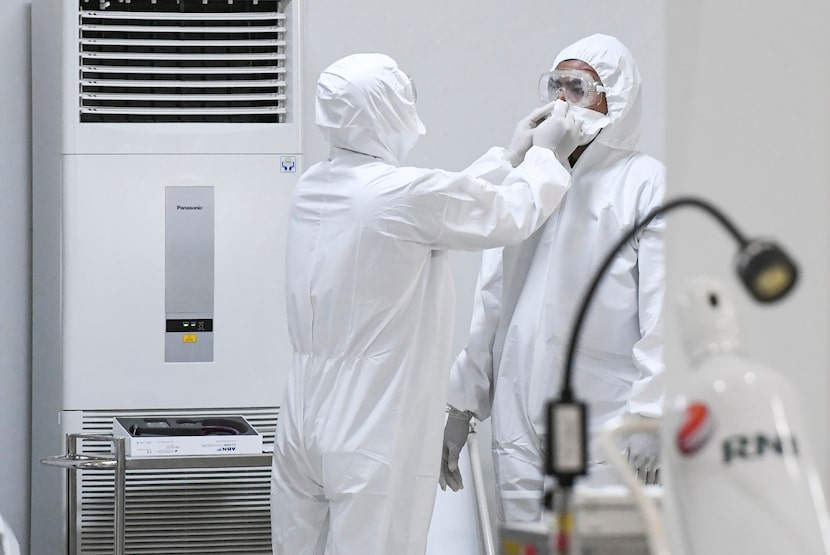 A staff member helps a colleague don his protective gears at an emergency hospital set up...