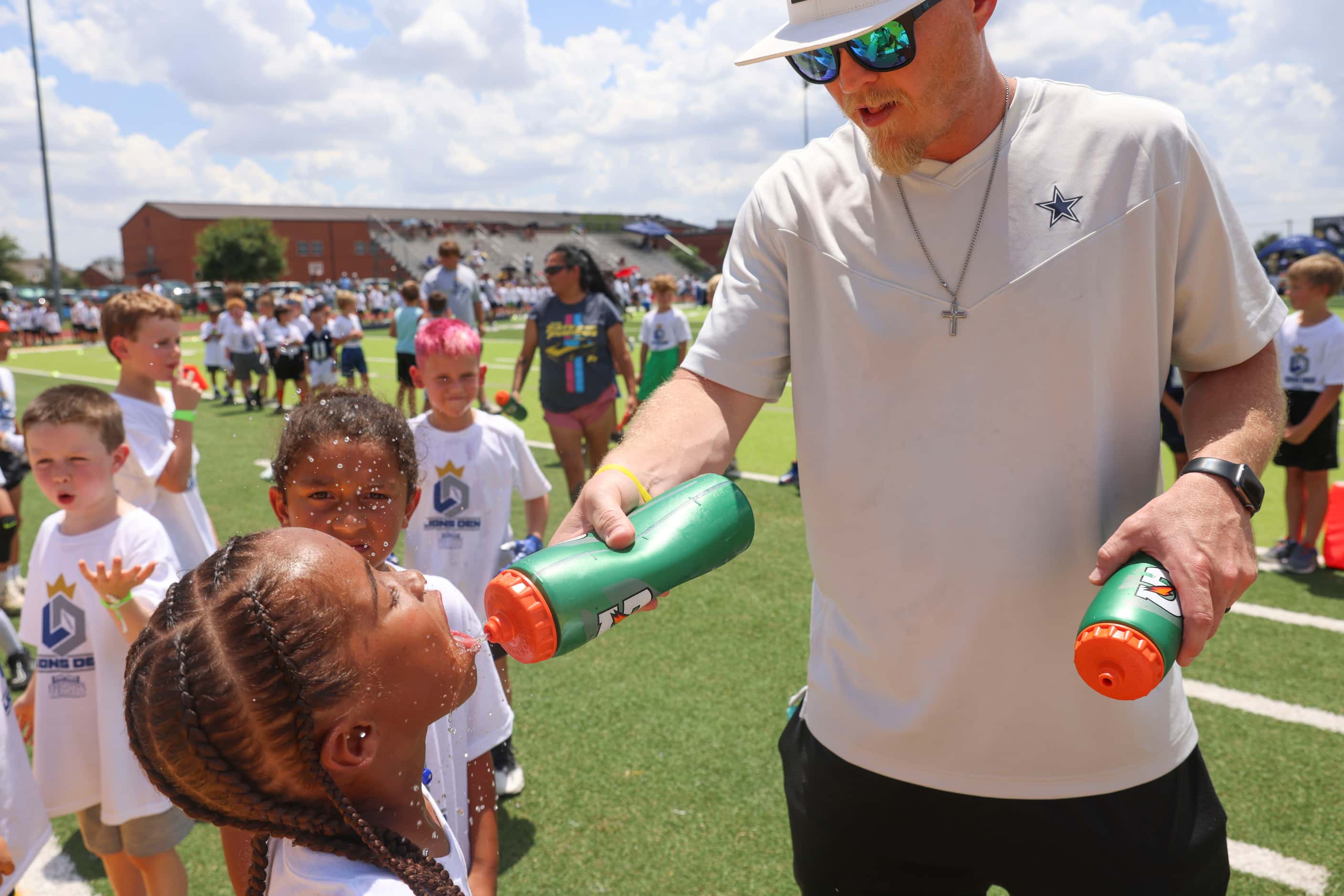 Volunteer Nathan Duran (right) sprays water on young football players as they line up to...