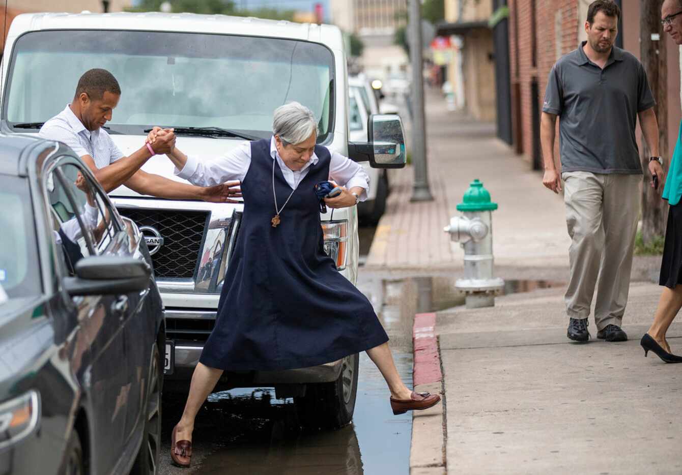 Sister Norma Pimentel gets a hand as she jumps over puddles on the curb in front of the...