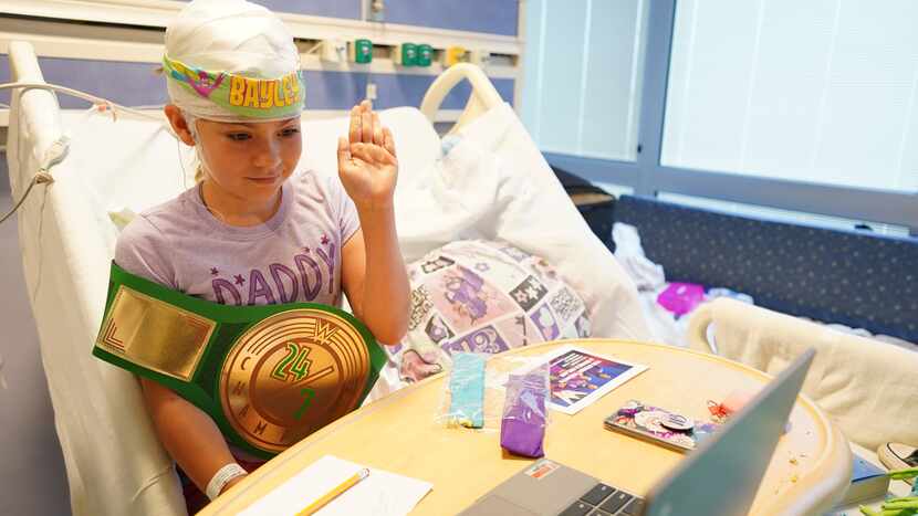 A young patient holding a WWE championship belt on a virtual Zoom call with WWE stars Montez...