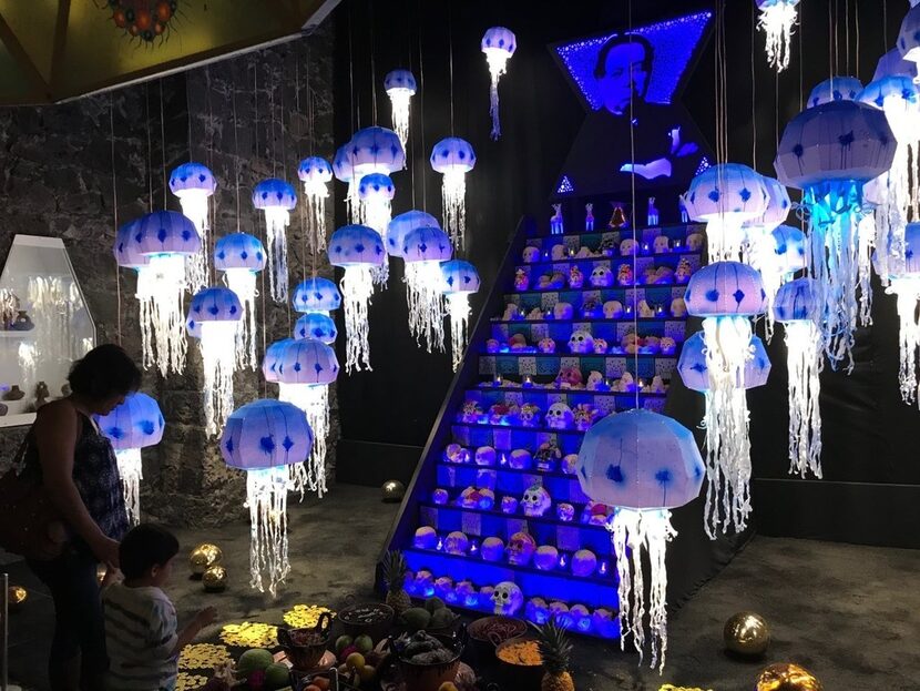 A woman bends over to talk with a child as they look at a Day of the Dead altar placed...