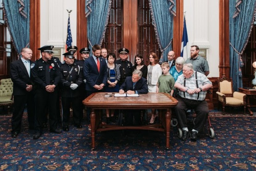 Gov. Greg Abbott, surrounded by Richardson-area lawmakers, and David Sherrard's parents,...