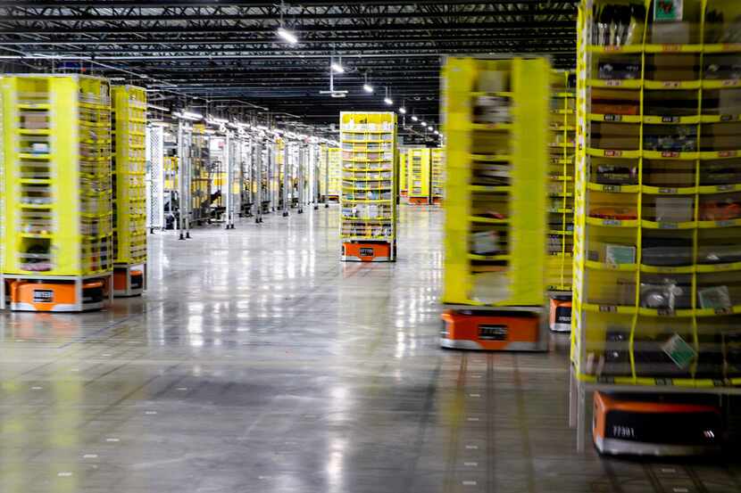 Robots carrying tall pods loaded with Amazon products move packages throughout an Amazon...
