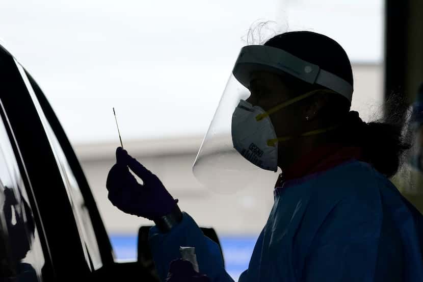 A healthcare worker holds up a swab after testing a passenger at a free COVID testing site...