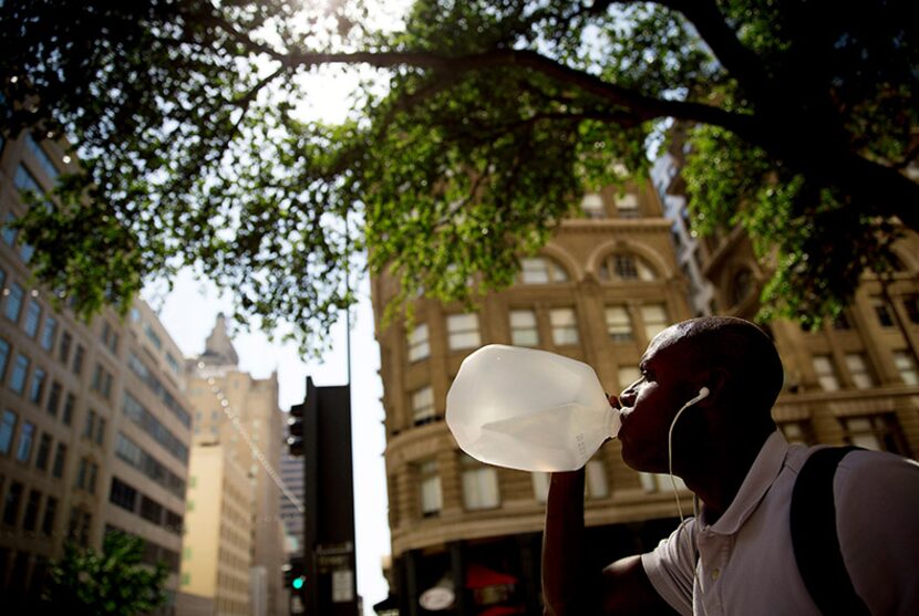  Ron Clemons drinks from a gallon water jug as he waits in the shade of a downtown tree for...