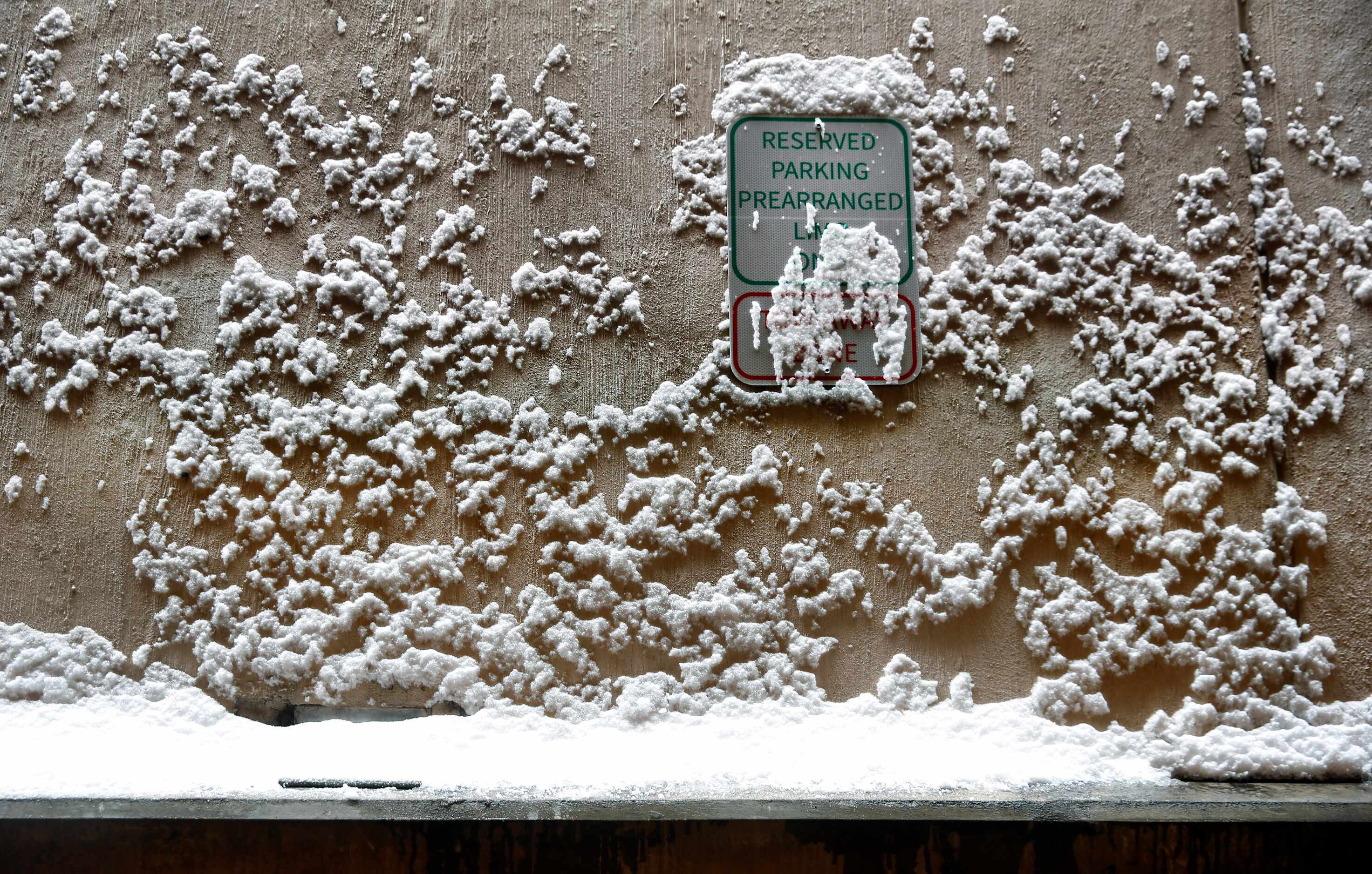 Snow clings to a parking sign and concrete wall in a DFW Airport terminal parking garage,...