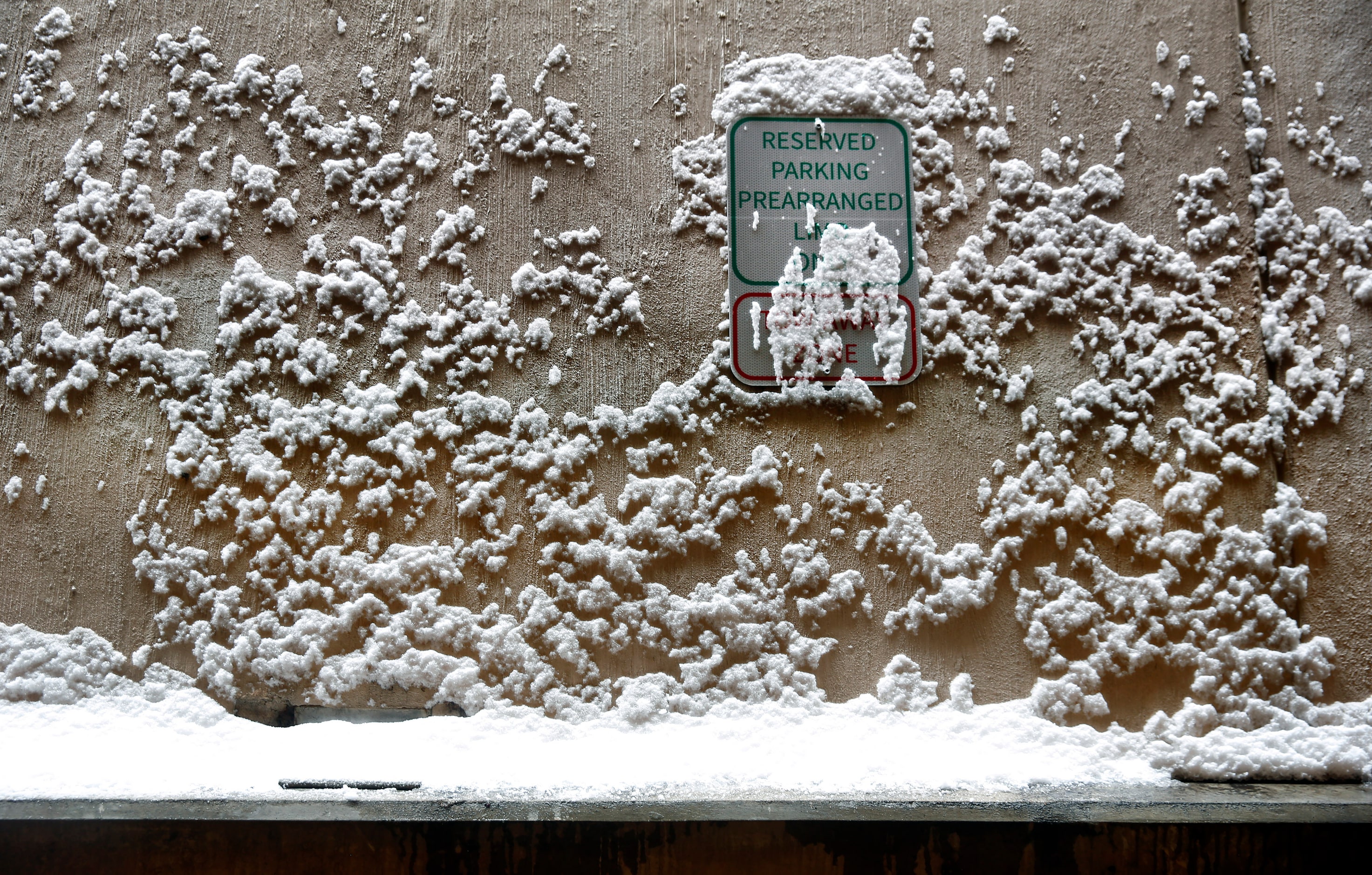 Snow clings to a parking sign and concrete wall in a DFW Airport terminal parking garage,...