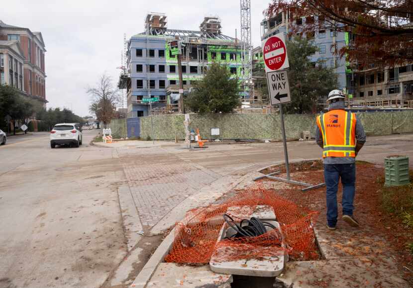 A construction worker walks by a hole in the sidewalk at the intersection of Reagan Street...