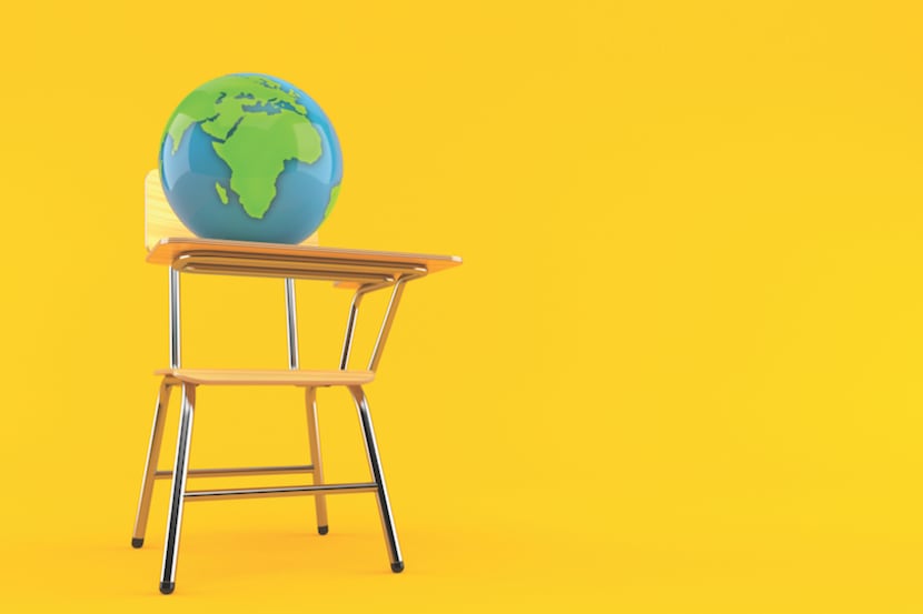 A globe sits on top of a school desk against a yellow background.