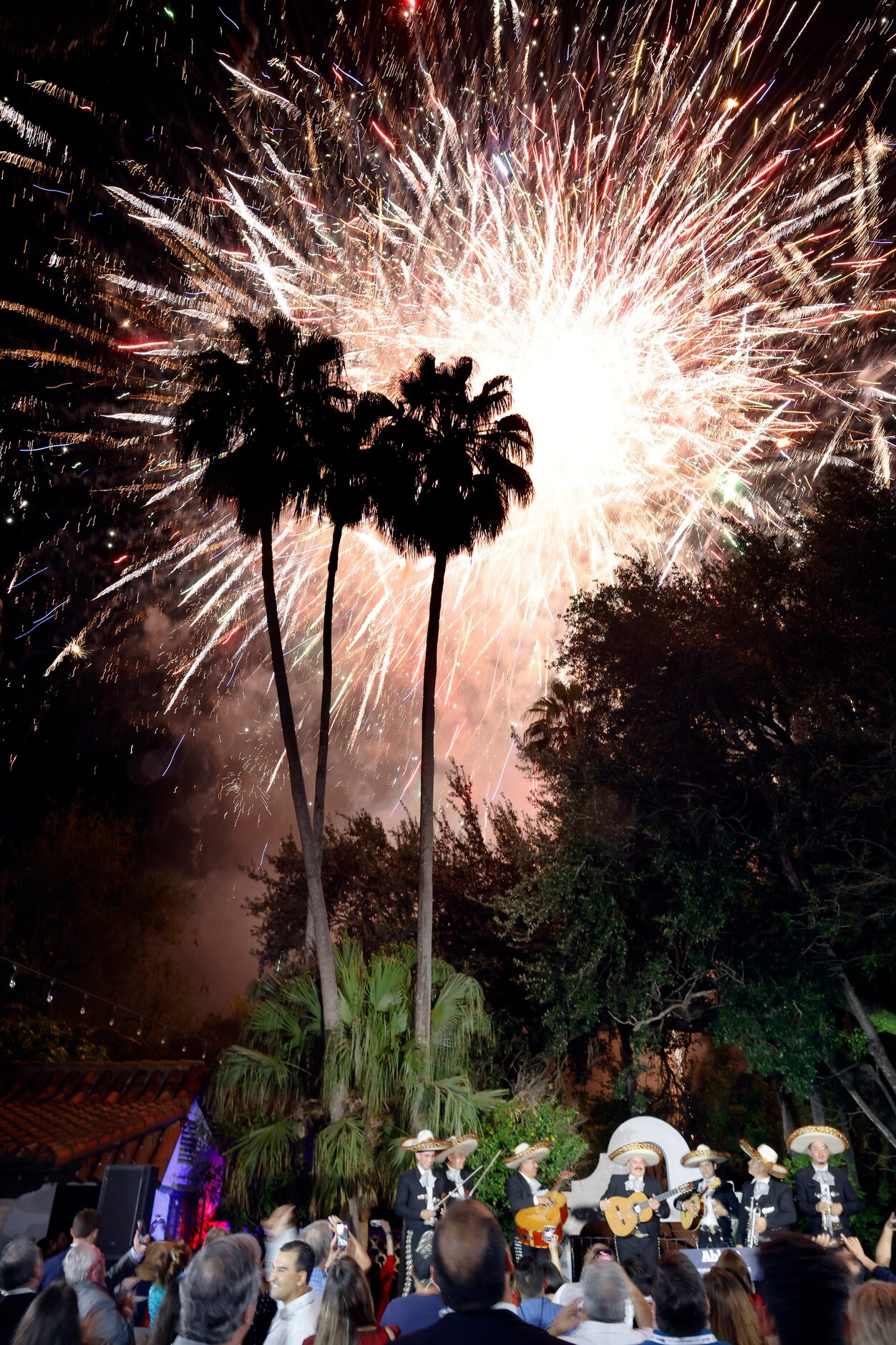 The grand finale of a fireworks show commences above a mariachi group playing following...