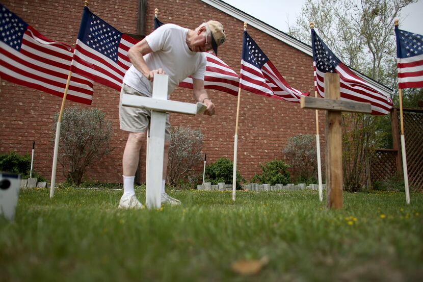 KILLEEN, TX - APRIL 03:  Bob Gordon paints a cross placed in front of 16 American flags as...
