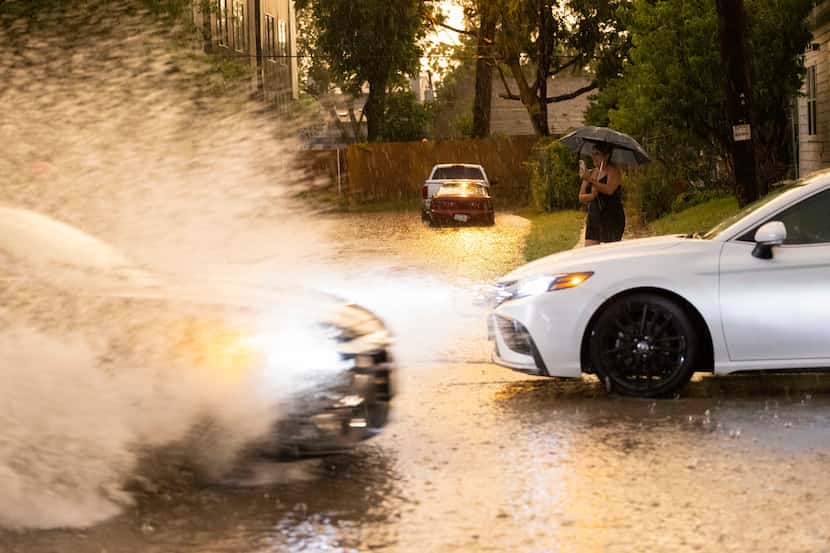 Rocio Acevedo stands at the corner as she watches cars pass through a flooded section of the...