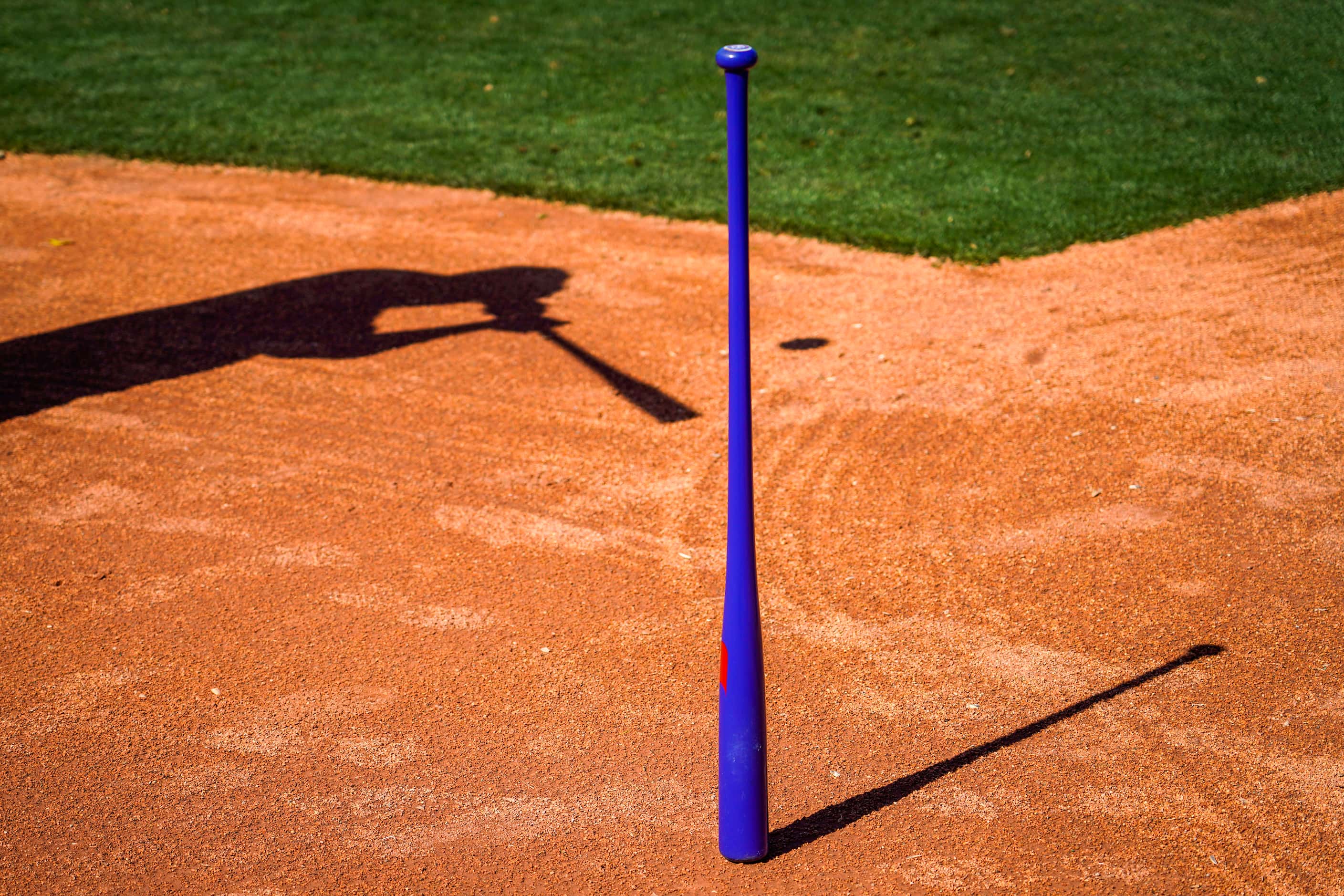 A fungo bat stands near home plate as Steve Buechele casts a shadow while hitting grounders...