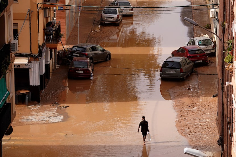 A man carrying water walks through flooded streets in Valencia, Spain, Wednesday, Oct. 30,...