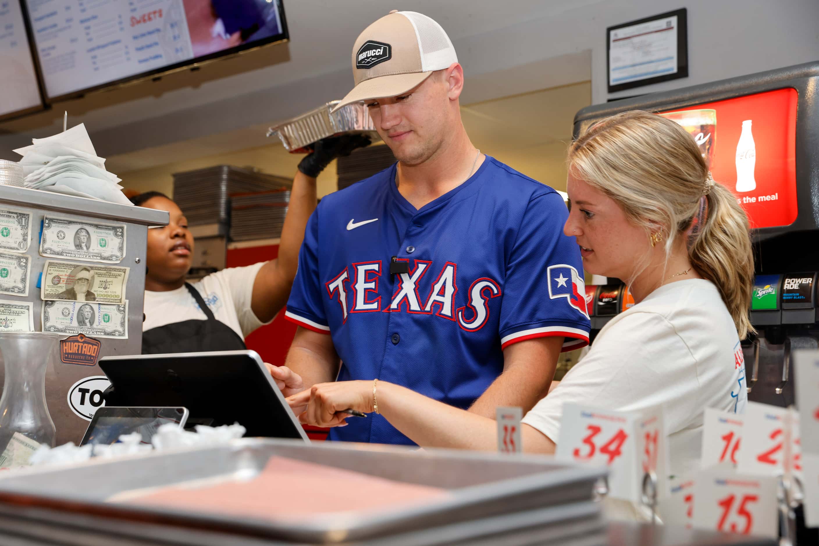 Texas Rangers third baseman Josh Jung learns how to use the register from Lauren McManus at...