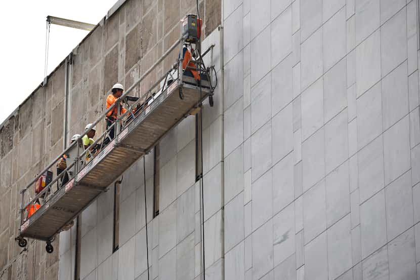 Construction workers use a scaffold to install marble on the First National Bank building in...