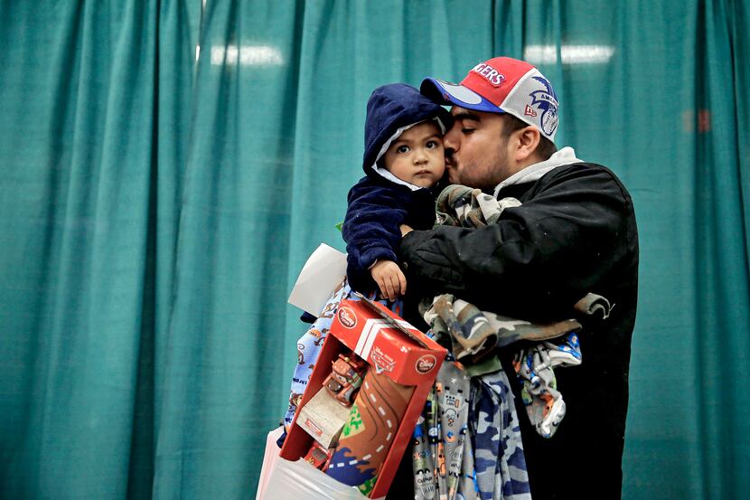 Jose Gonzalez holds donated gifts as he kisses his son Kareem, 1, during the "Christmas Gift...