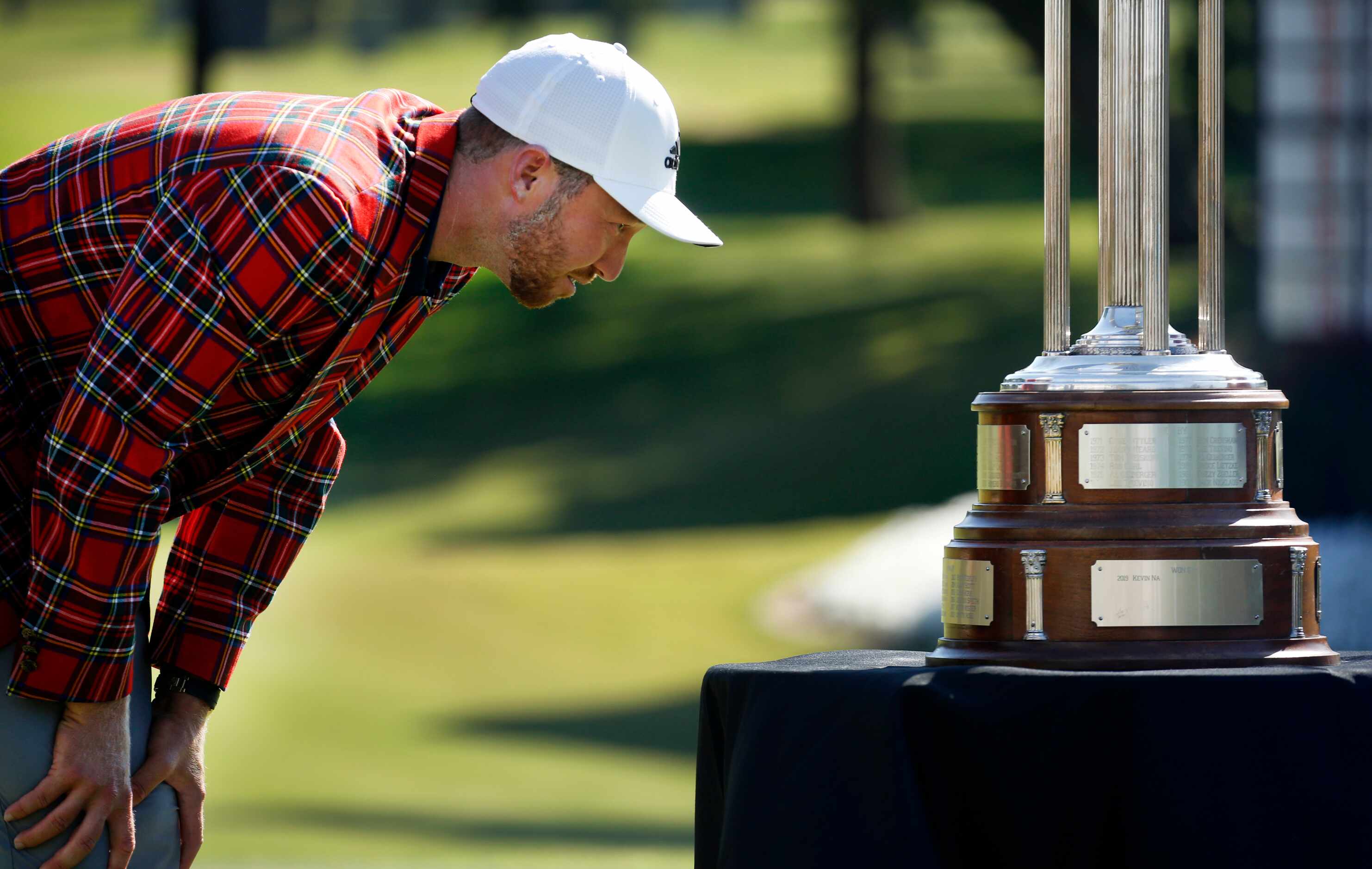 On the 18th green, PGA Tour golfer Daniel Berger looks at past winners on the Leonard Trophy...