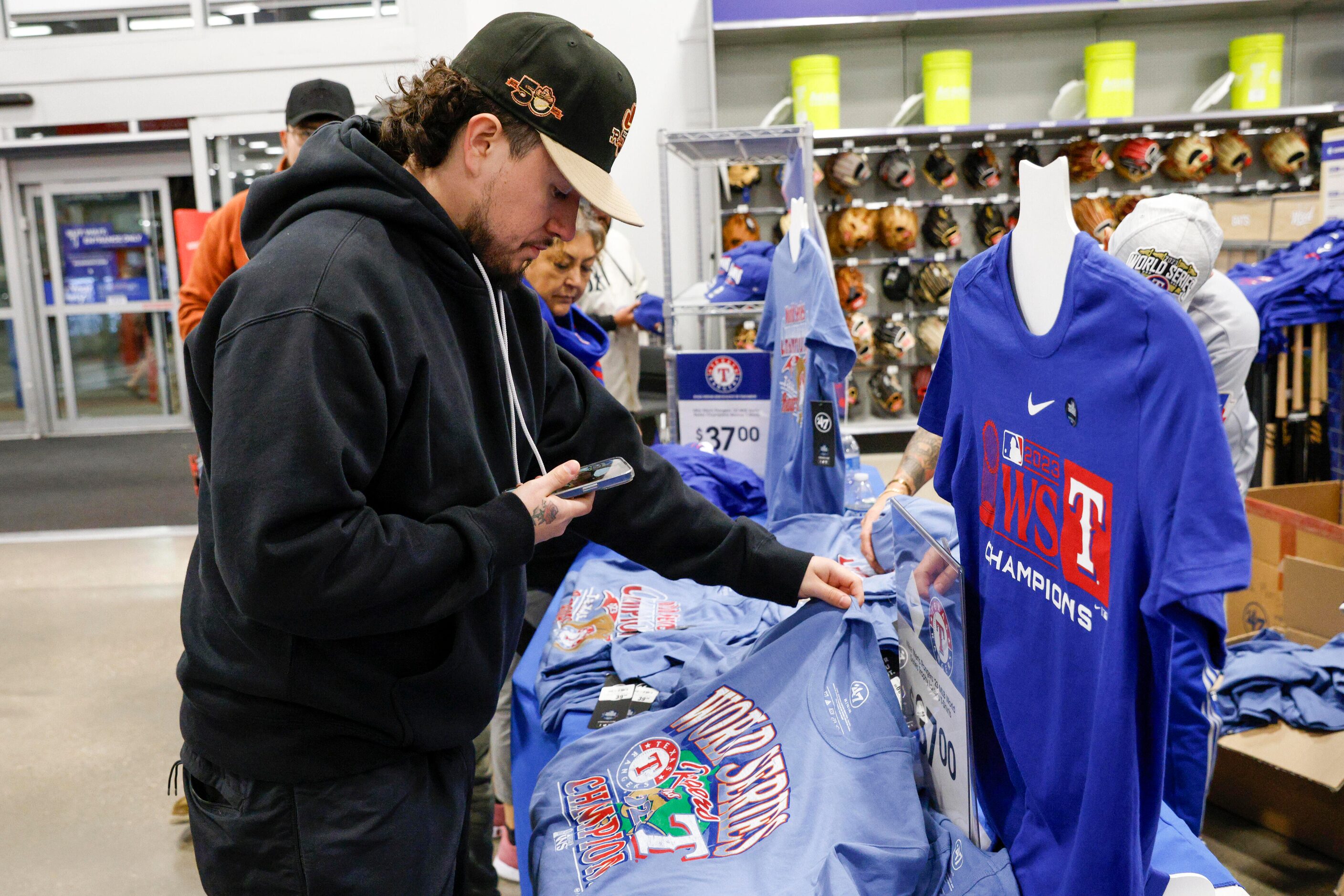 Juan Guerra looks at Texas Rangers World Series championship shirts as he talks on FaceTime...