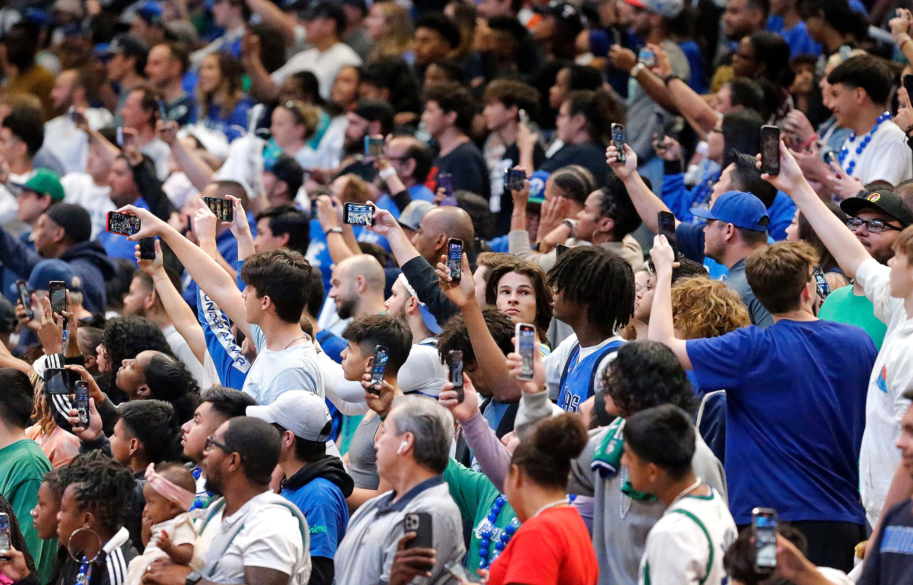 Fans in attendance hold up their phones to record the team taking the court for the first...