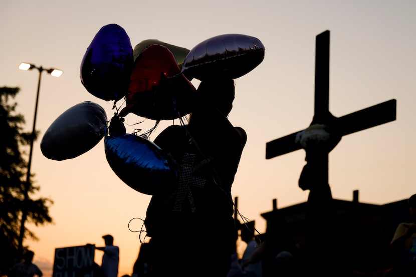 Attendees carrying balloons pass by the memorial outside of the Allen Premium Outlets mall...