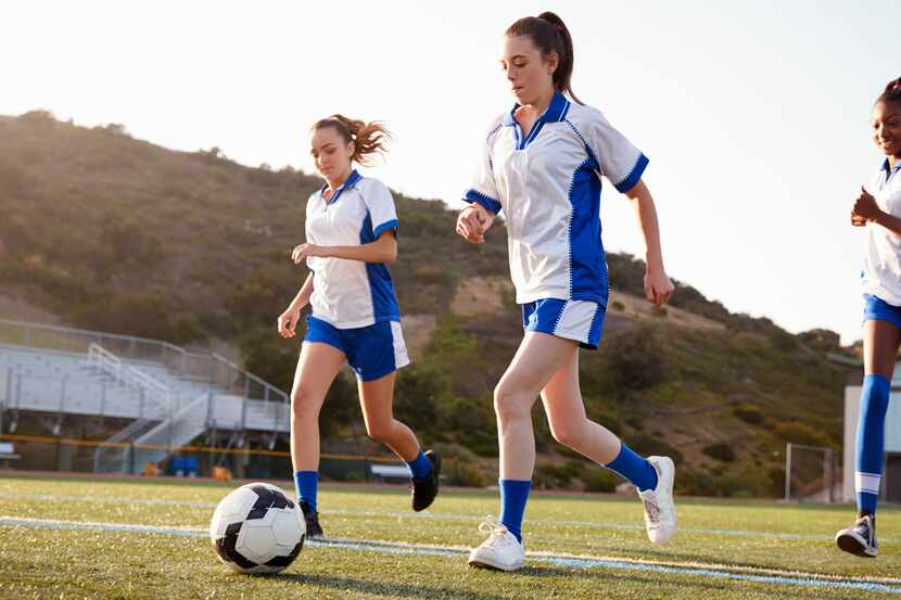 Group of three teenage girls playing soccer on a field while wearing uniforms.