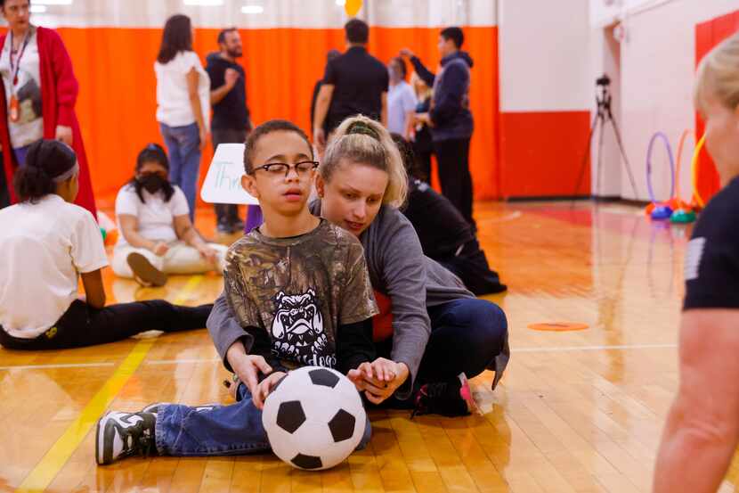 Malachi Jackson (left), 16, is guided in catching a soccer ball by Abby Blackwell, a Dallas...