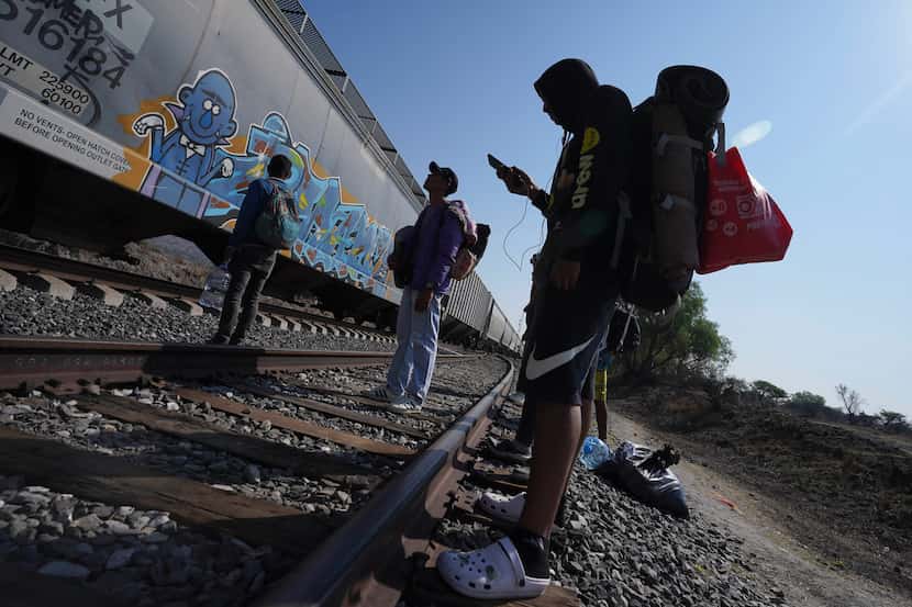 Migrantes miran un tren pasar mientras esperan en las vías con la esperanza de poder abordar...