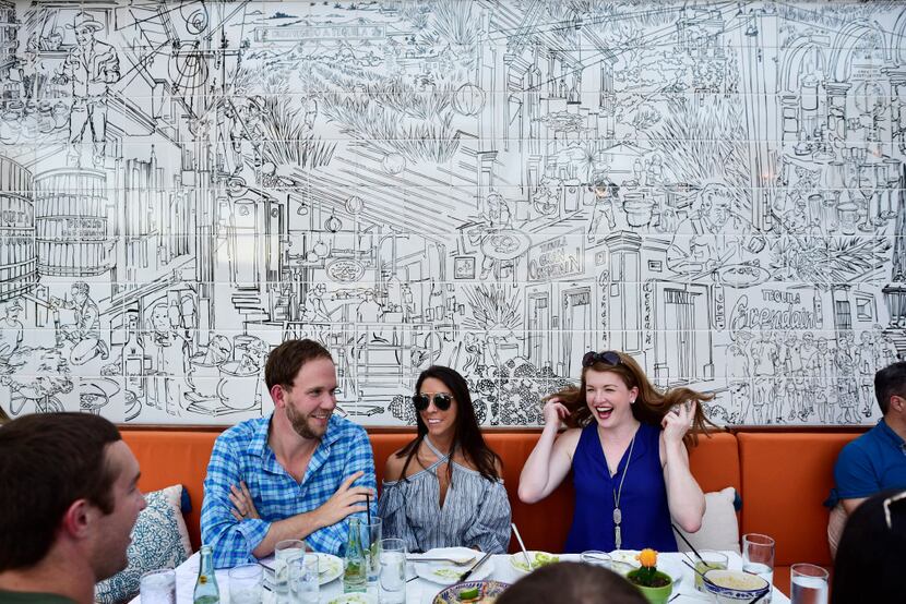 On the patio at Jose, diners are seated at a table backed by a black-and-white tile mural by...