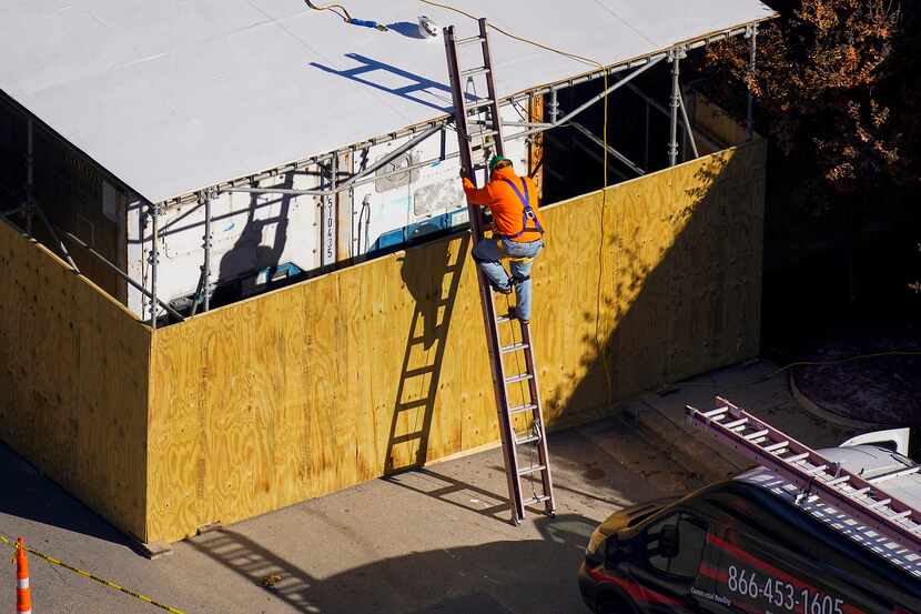 Workers construct a temporary structure around refrigerated trucks on the curbside next to...