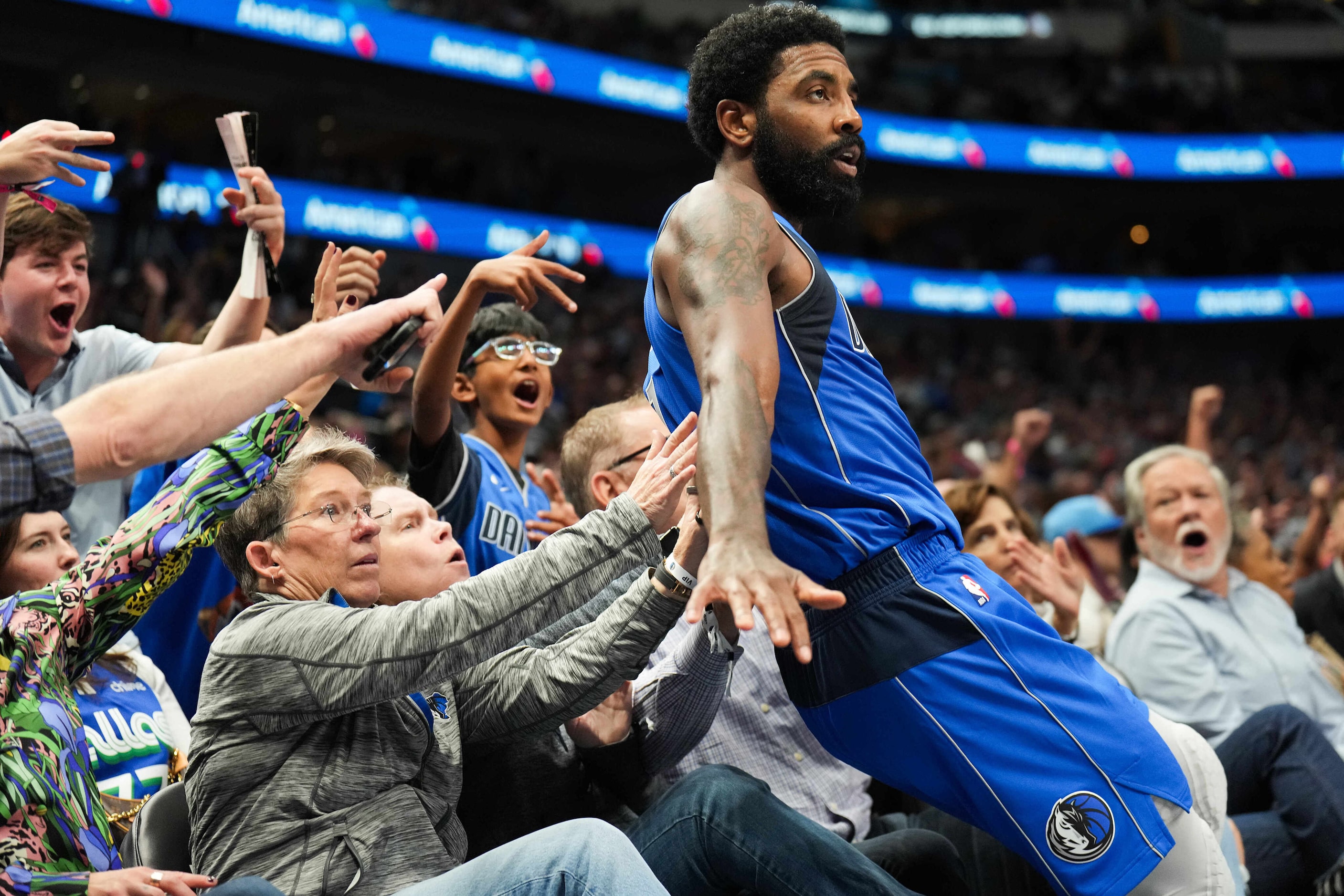 Dallas Mavericks guard Kyrie Irving tumbles into the crowd after hitting a 3-pointer during...