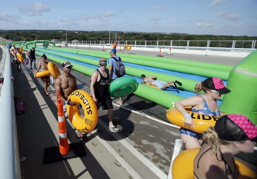 Water sliders walk back to the top of a 1,000 foot water slide during the Slide the City...