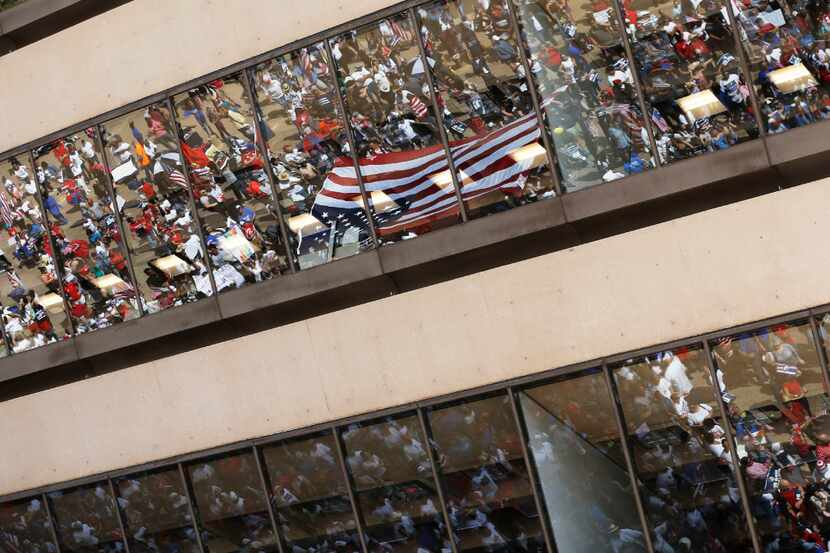 Reflection of a flag and people out in front of Dallas City Hall as speakers talk to the...